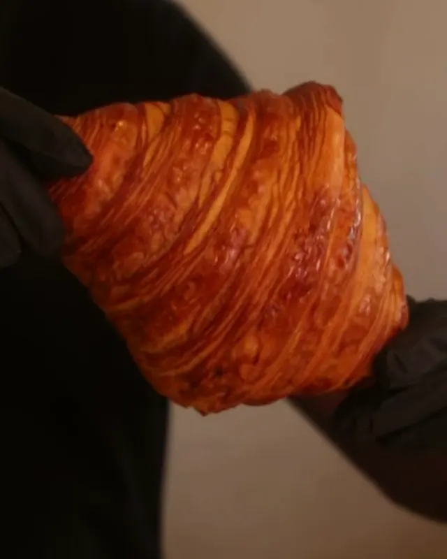 Croissant dorado sostenido con guantes, con sus capas de hojaldre a la vista